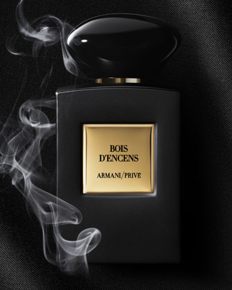 Photograph of a bottle of Giorgio Armani Sì resting on a red floor with a close-up of a slice of pear, vanilla pod and flower petals nearby