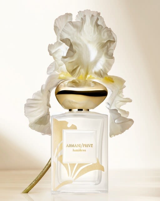 Photograph of a bottle of Giorgio Armani Sì resting on a red floor with a close-up of a slice of pear, vanilla pod and flower petals nearby